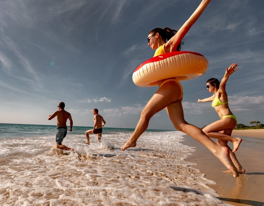 Four adults, two men and two ladies running towards the beach wearing bikinis and sunglasses - See Breeze Optometry Four adults, two men and two ladies running towards the beach wearing bikinis and sunglasses - See Breeze Optometry