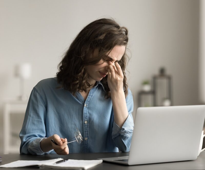Tired woman sit at desk, takes off glasses to relieve eye strain after long laptop usage, suffers from eyestrain or dry eyes, having headache, massage nose bridge. Vision issues, on-line work or study