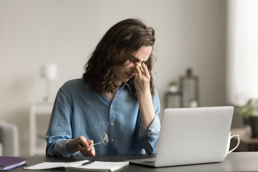 Tired woman sit at desk, takes off glasses to relieve eye strain after long laptop usage, suffers from eyestrain or dry eyes, having headache, massage nose bridge. Vision issues, on-line work or study
